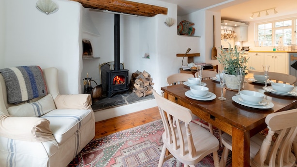 Un salon chaleureux avec une cheminée, un coin repas avec une table et des chaises en bois, et une cuisine visible au fond.