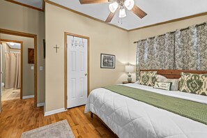 A bedroom with a bed, a ceiling fan, a door, a framed picture, and a patterned curtain.