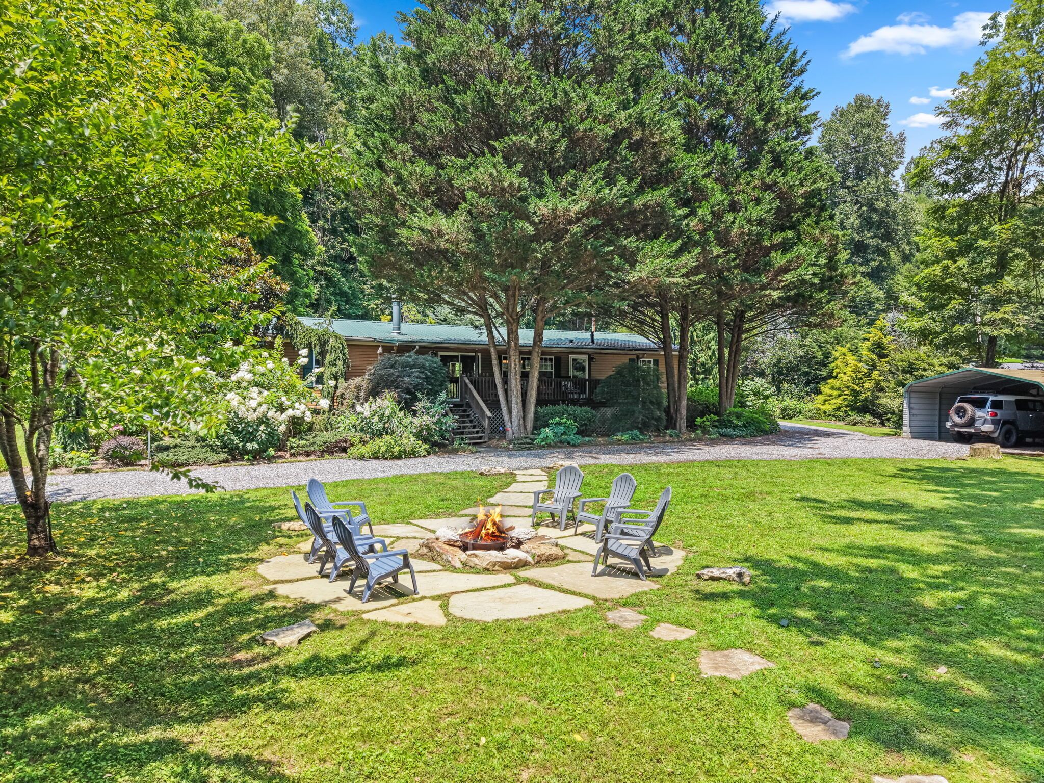 A backyard with a stone fire pit, outdoor seating, and a house with a green roof.