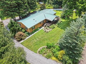 A two-story house with a green roof, surrounded by a well-maintained lawn and trees.