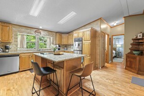 A kitchen with wooden cabinets, a granite countertop, a stainless steel refrigerator, and two bar stools.