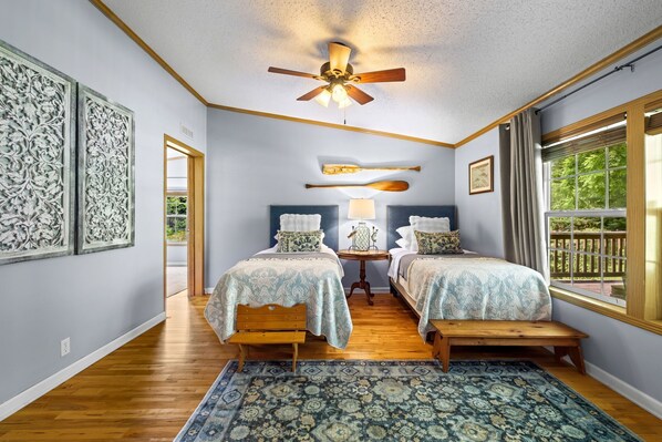 A bedroom with two beds, a ceiling fan, a window with a view, and a patterned rug.