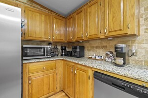 Eine Küche mit Holzausstattung, einem Edelstahlkühlschrank, einer Mikrowelle, einer Kaffeemaschine und einem Geschirrspüler.