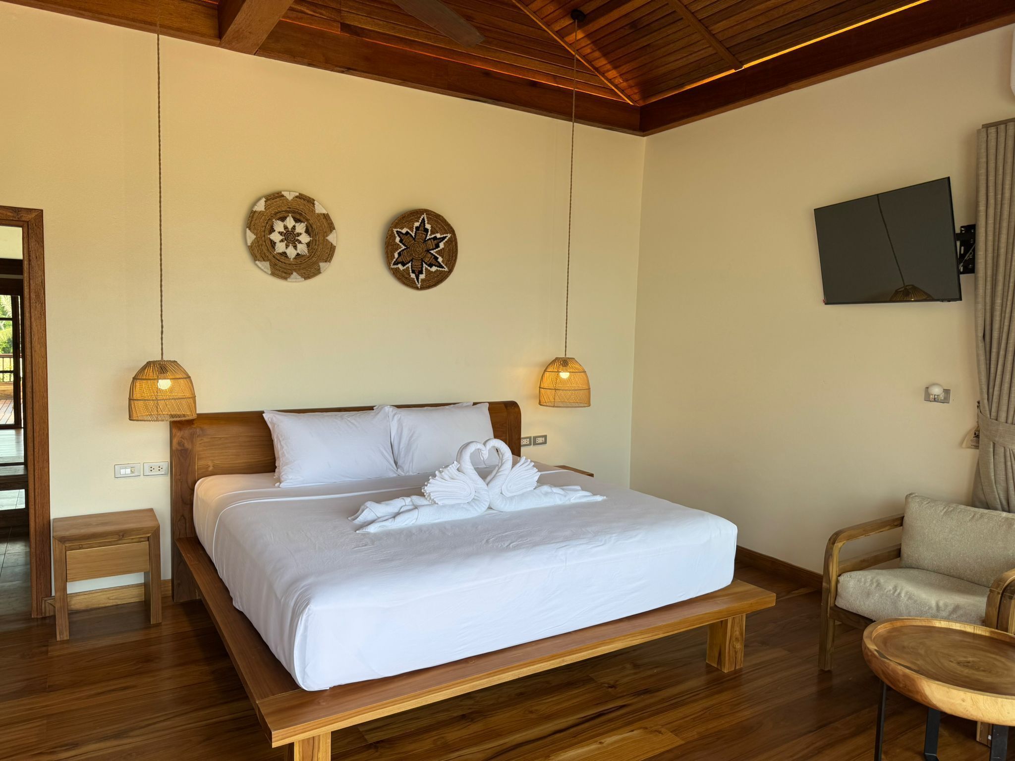 A bedroom with a wooden bed, two wall-mounted lamps, a flat-screen TV, and a wooden chair.