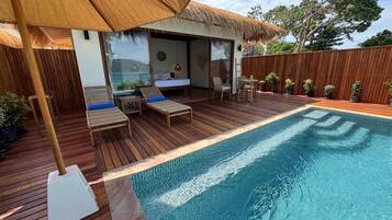 A wooden deck with a pool, lounge chairs, and a thatched roof structure.