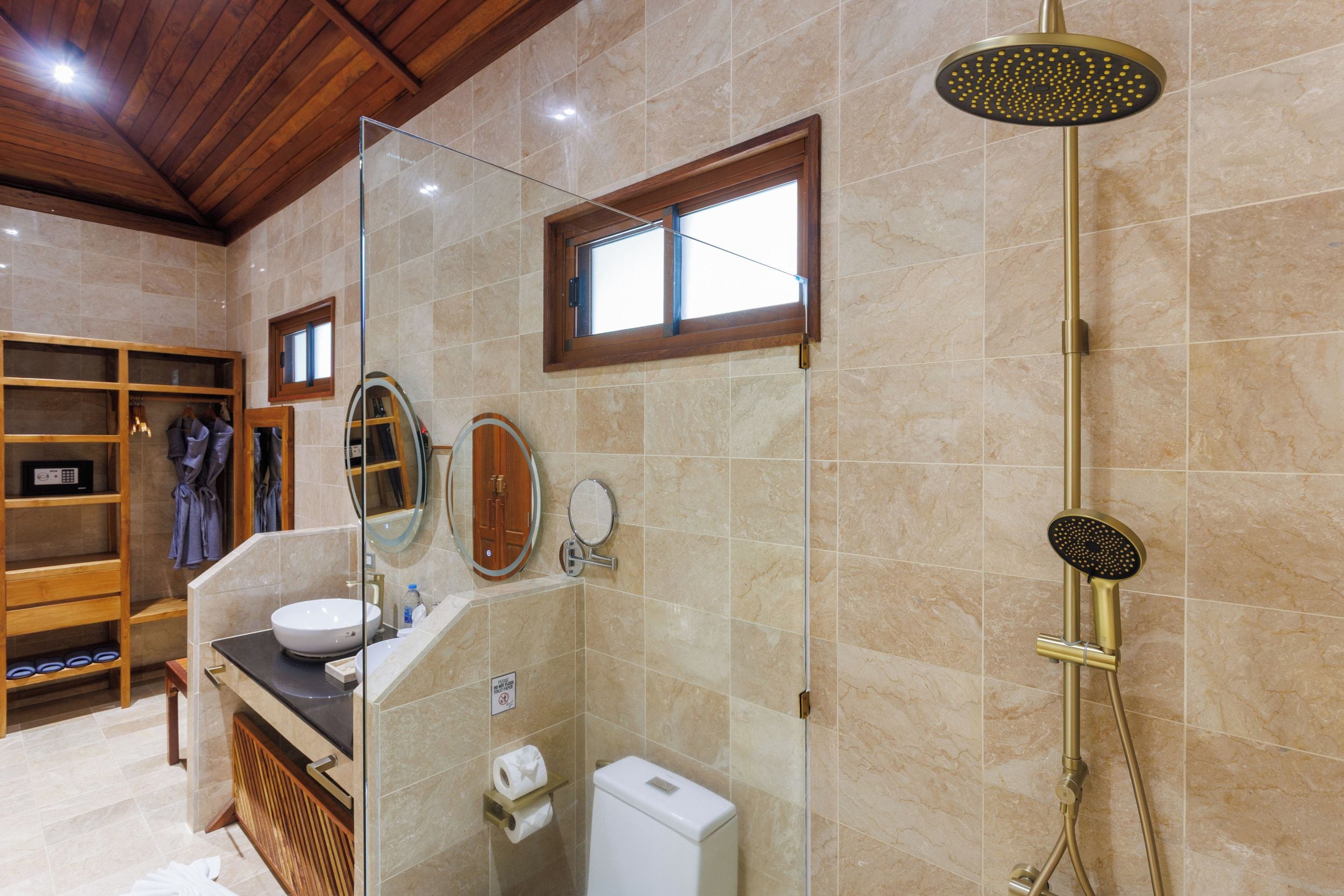 Un baño moderno con ducha envuelta en vidrio, tocador de madera, inodoro y barra para toallas.
