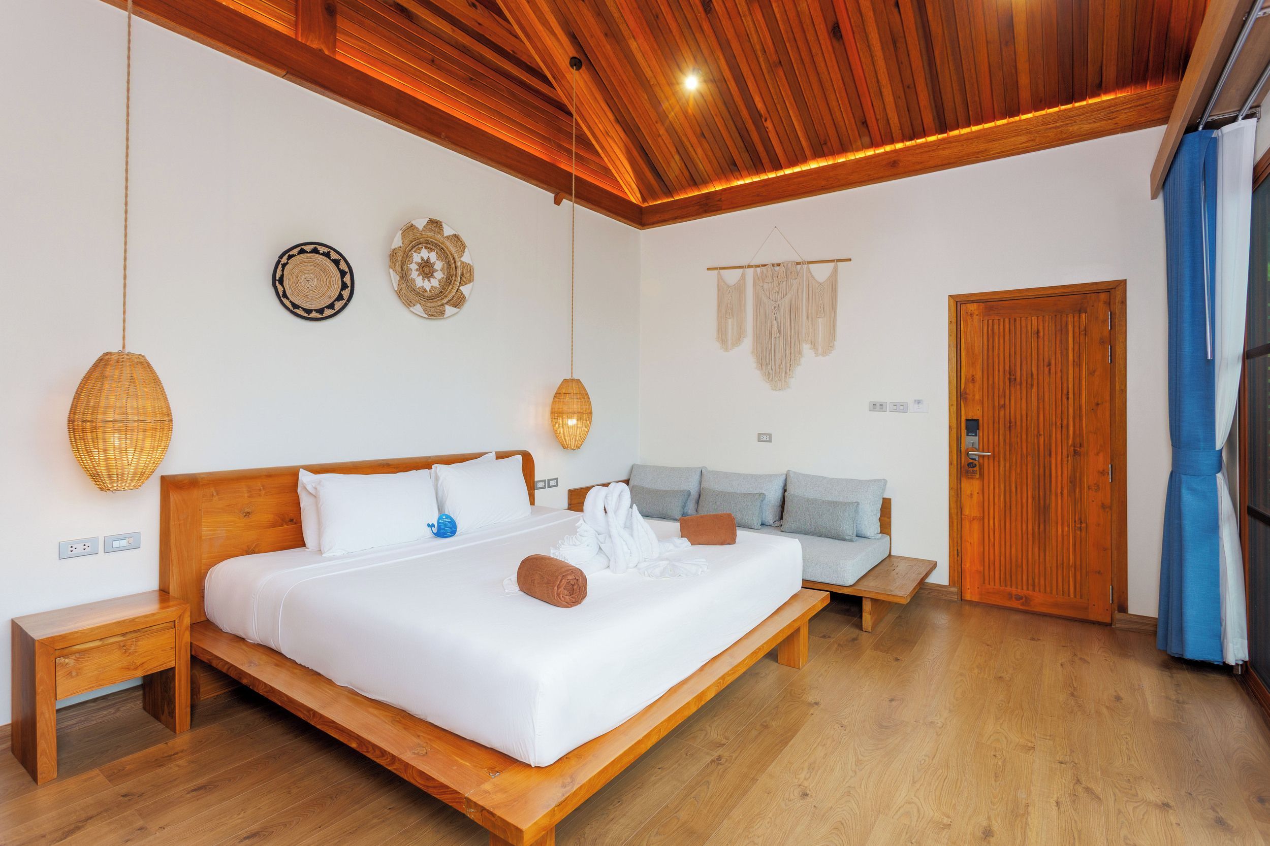Una habitación de hotel con una cama de madera, un sofá, una lámpara colgante y una puerta de madera.