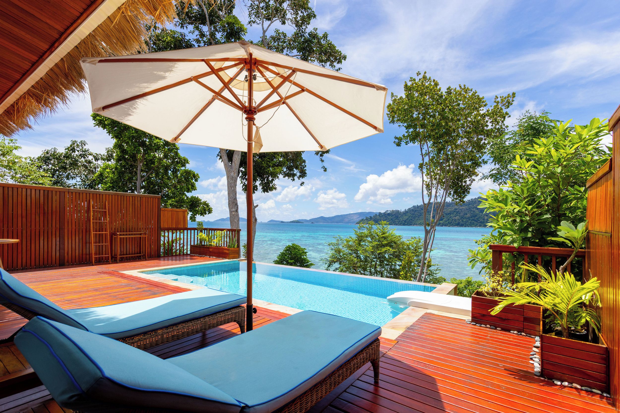 A poolside area with a lounge chair, a large umbrella, and a view of the sea.