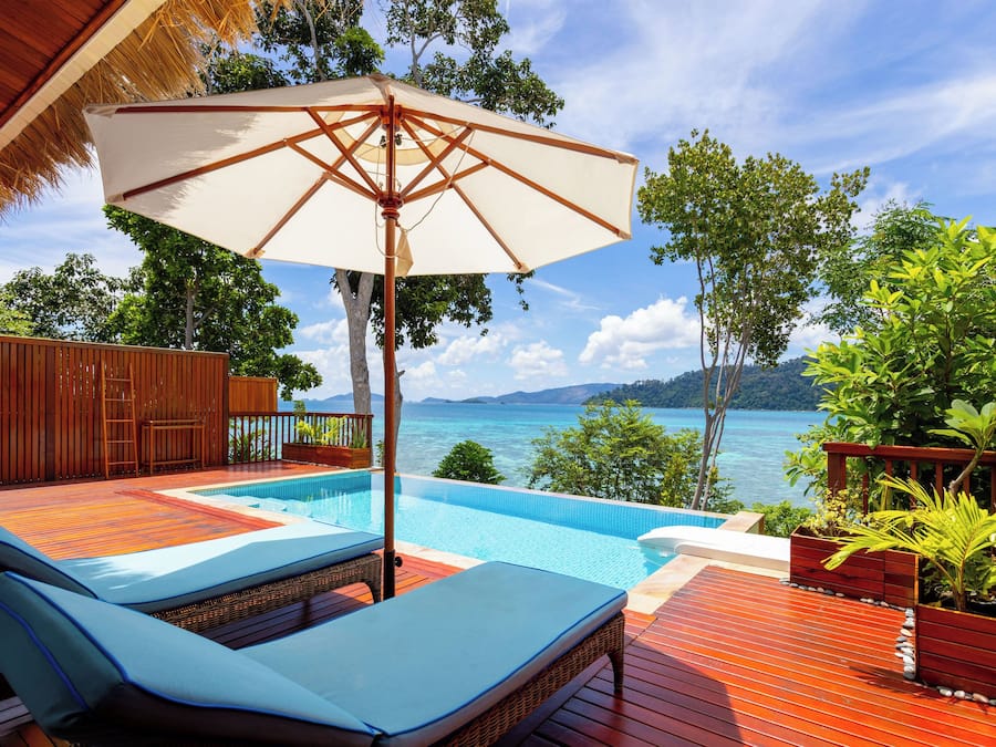 Zona de piscina con una tumbona, una sombrilla grande y vista al mar.