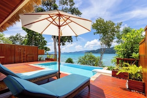 A poolside area with a lounge chair, a large umbrella, and a view of the sea.