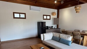 A modern living room with a sofa, wooden coffee table, and a dining area with wicker chairs. - Ten Moons Sunset Villas (Koh Lipe)