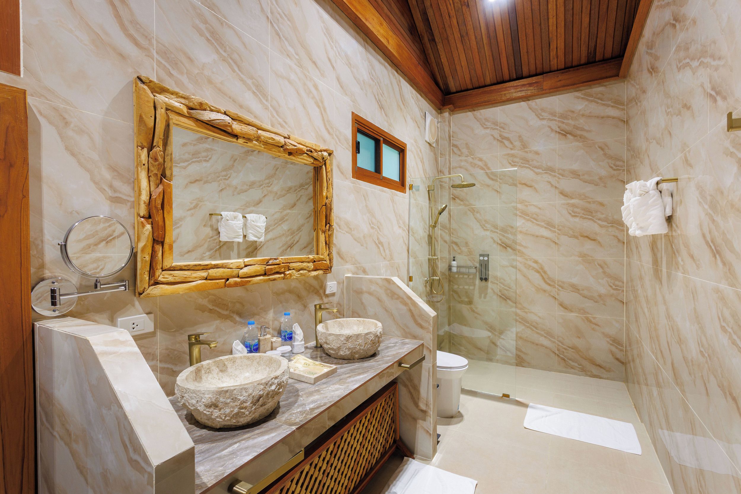 Une salle de bain dotée d’un grand miroir, de deux vasques en pierre, d’une douche à parois de verre et de murs en marbre.