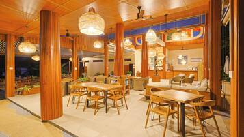 A spacious indoor area with wooden furniture, including tables and chairs, and hanging pendant lights.
