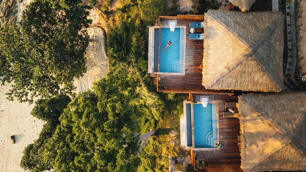 An aerial view of a resort with two separate swimming pools, wooden deck areas, and thatched-roof structures. - Ten Moons Sunset Villas (Koh Lipe)