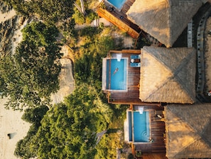 An aerial view of a resort with two separate swimming pools, wooden deck areas, and thatched-roof structures.