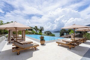 A poolside area with lounge chairs and umbrellas, overlooking a body of water and greenery.