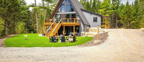 Une cabane moderne dotée d’une grande terrasse, entourée d’une forêt.