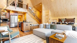 Un vaste espace de vie de style loft, doté d’un plafond haut, d’une mezzanine accessible par un escalier, d’une cuisine moderne et d’un coin repas offrant une vue agréable.
