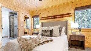 Une chambre à coucher aux murs lambrissés, avec un grand lit, deux tables de chevet dotées de lampes et une vue sur l’extérieur par une fenêtre.