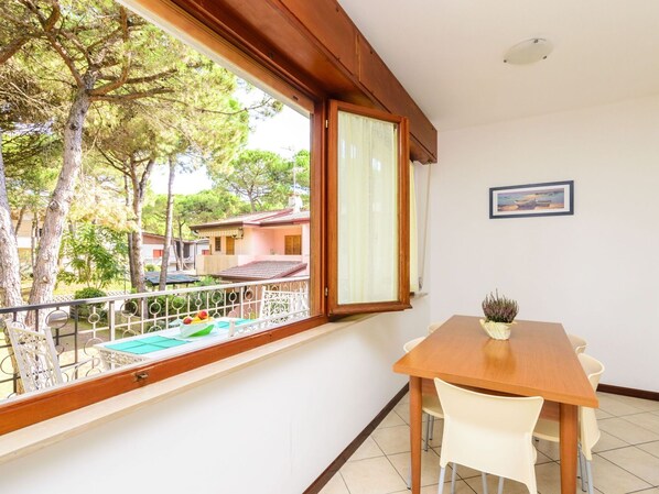 A balcony with a wooden table and chairs, a view of trees and buildings, and a framed picture on the wall.
