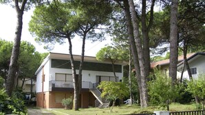A two-story building with a staircase leading to a balcony, surrounded by trees and a gated entrance. - Nice apartment for 7 people with A/C, WIFI, TV, terrace and pets allowed (Lignano Sabbiadoro)