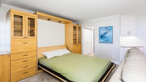 Une chambre à coucher avec un lit, une armoire en bois avec des tiroirs, une porte et un tableau au mur.