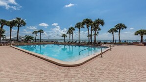 A rectangular swimming pool with a tiled deck surrounding it, palm trees, and a view of the water.