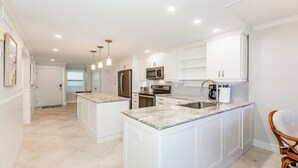 A modern kitchen with white cabinetry, a marble countertop, stainless steel appliances, and pendant lighting.