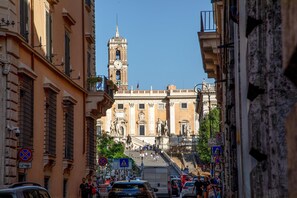 A street leading to a historic building with a clock tower, statues, and a staircase.