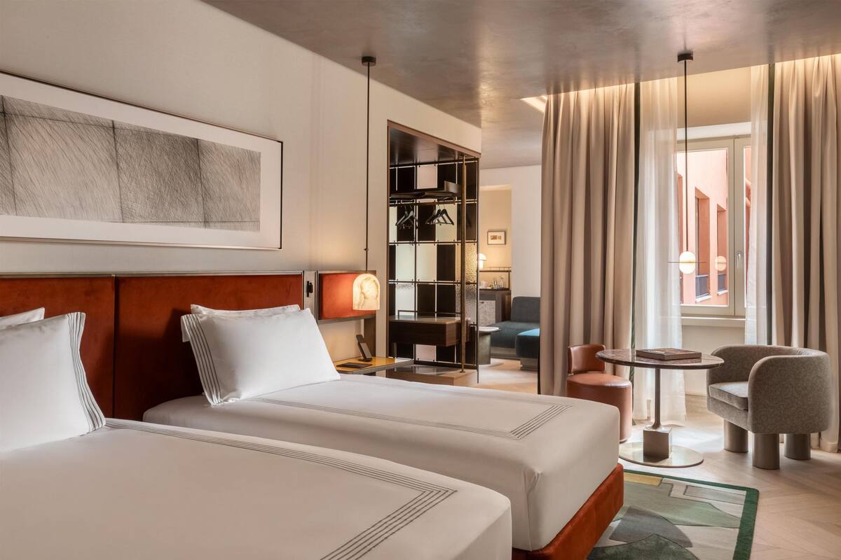 A hotel room with two beds, a desk, a chair, a small table, and a view of the outside.