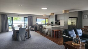 A modern kitchen with grey cabinets, stainless steel appliances, and a bar area. There is a dining area with grey chairs and a table, and a living room with a leather sofa and a decorative glass dome. - Waterfront & spacious. Room for cars & boat trailer. 6KM from Havelock Marina (Havelock)