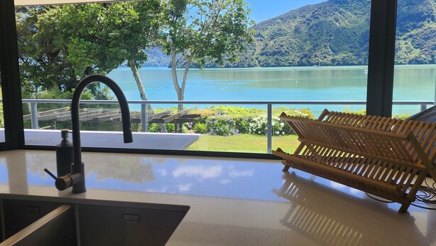 A modern kitchen with a sink and a wooden bench by a large window overlooking a lake and mountains. - Waterfront & spacious. Room for cars & boat trailer. 6KM from Havelock Marina (Havelock)