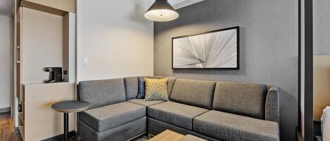 A modern living room with a sectional sofa, a small round table, and a coffee machine.