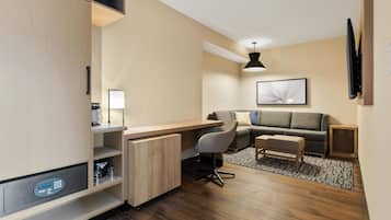 A compact, modern room with a built-in desk, a comfortable sofa, a small table, and a ceiling light.