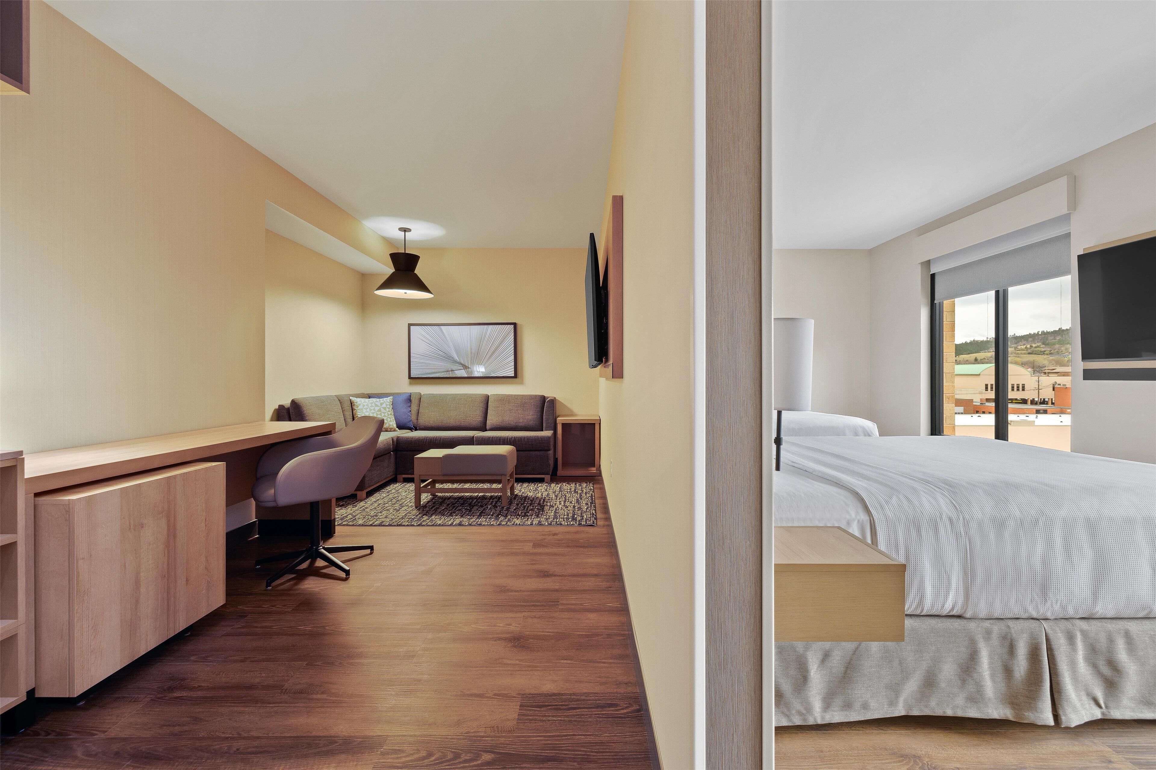 Ein modernes Hotelzimmer mit einem Holztisch, einer Couch, einem Bett und einem großen Fenster mit Blick.