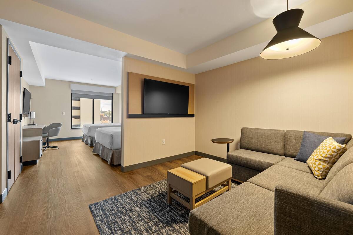 Una sala de estar moderna con un sofá, un reposapiés y un televisor de pantalla plana montado en la pared.