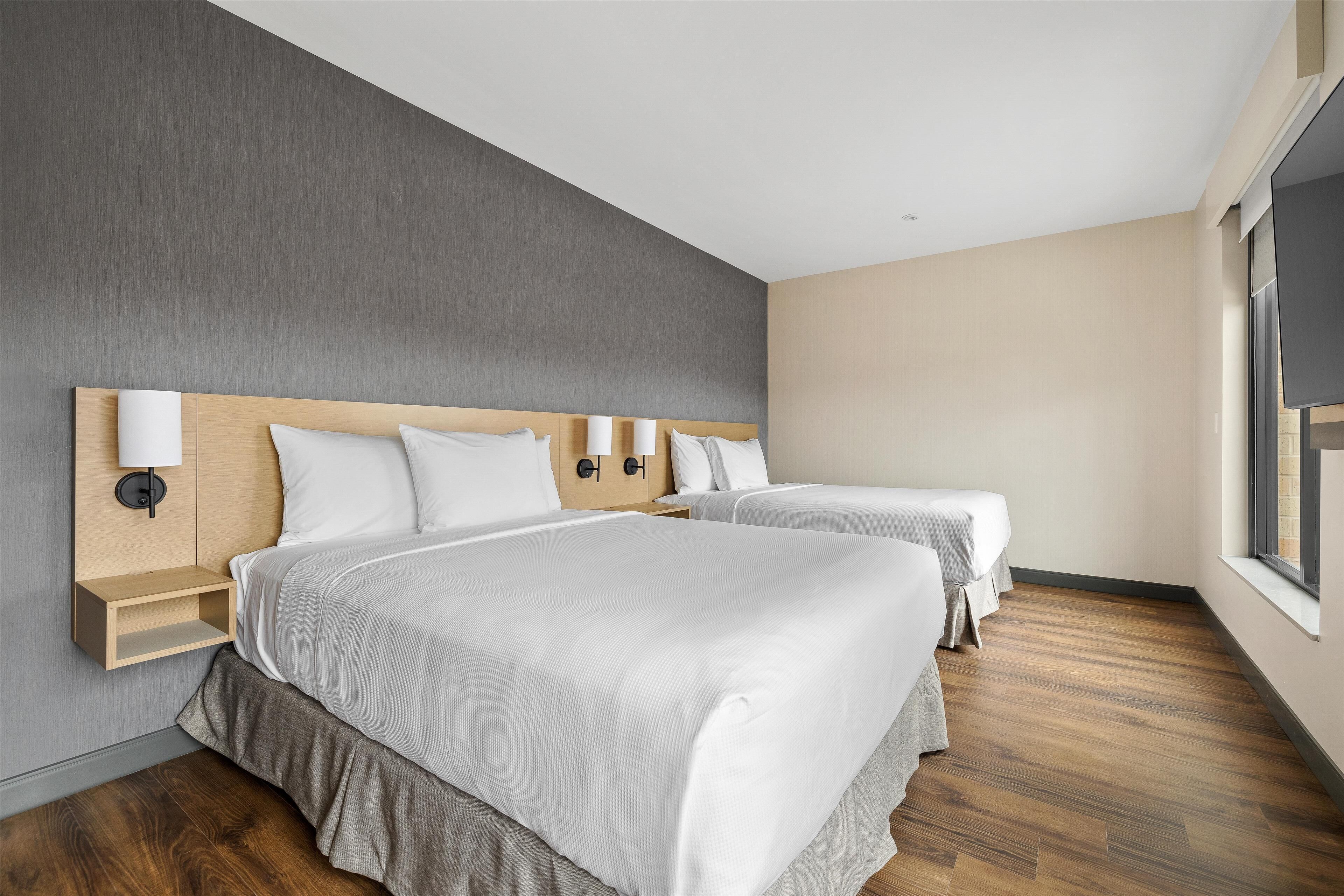 A hotel room with two beds, a wooden headboard, a nightstand, and a window.