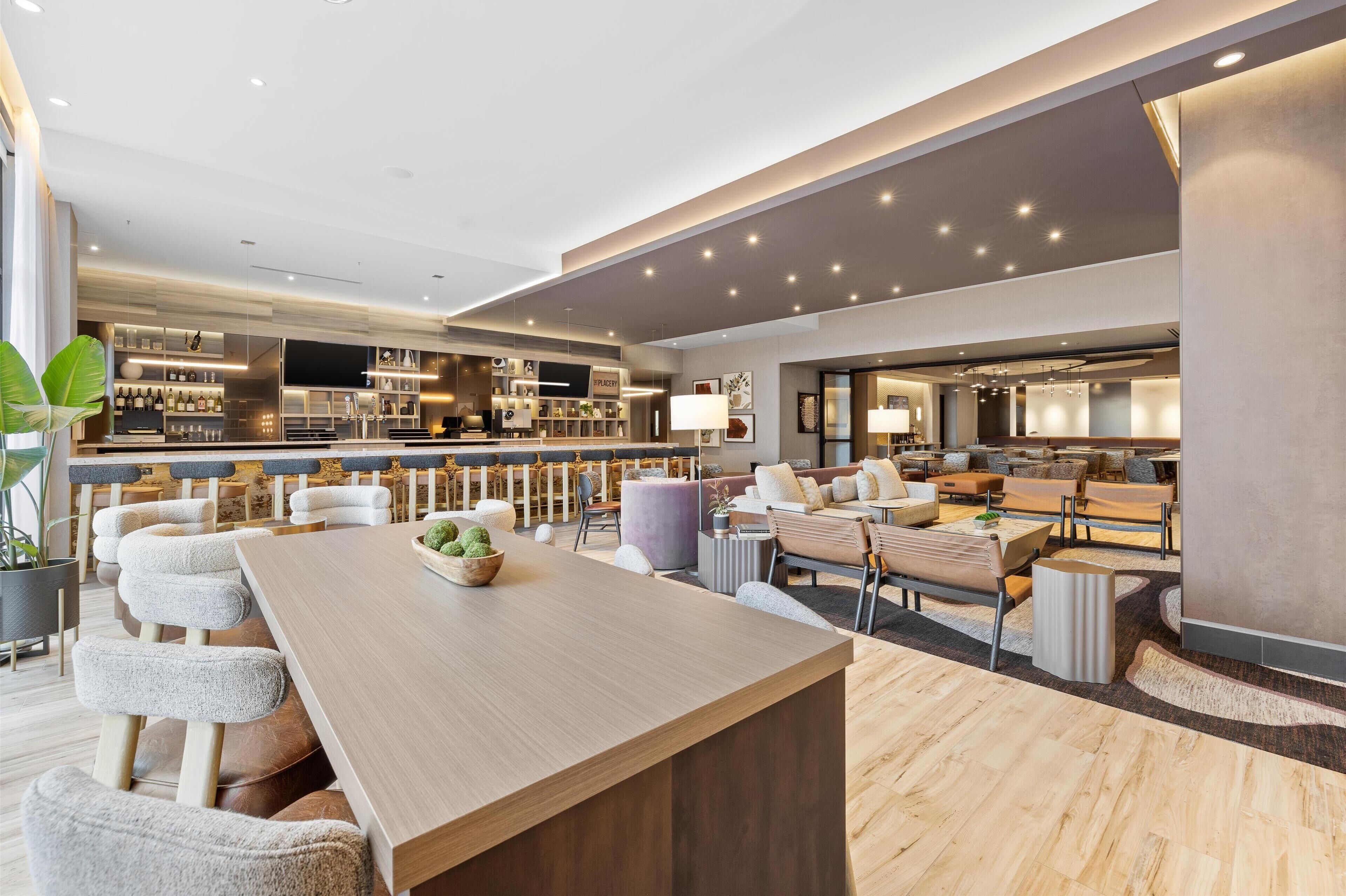 A modern bar area with a long counter, bar stools, and a variety of bottles.