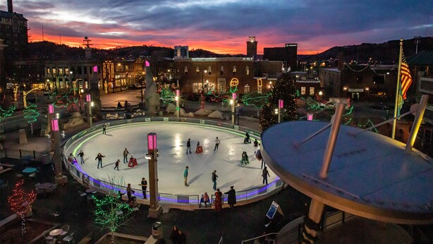An outdoor ice skating rink surrounded by buildings with holiday decorations. - Hyatt Place Rapid City / Downtown (Rapid City)
