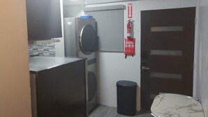 A compact kitchen with a washing machine, a fire extinguisher, and a trash bin.