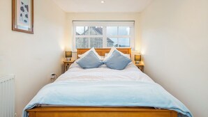 A bedroom with a wooden bed, two bedside lamps, a window with a view, and a framed picture on the wall. - Llys Bonfyl, Holiday Cottage St Dogmaels, Sleeps 6, 3 bedrooms,  bathrooms (Cardigan)
