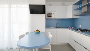 A modern kitchen with white cabinets, a blue countertop, a microwave, a gas stove, and a dining area with a table and chairs. - Lovely apartment for 4 people with A/C, WIFI, TV, balcony and pets allowed (Lignano Sabbiadoro)