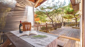 Une terrasse en bois agrémentée d’un panier en osier, d’une bouteille de vin et de deux verres posés sur une nappe en dentelle.