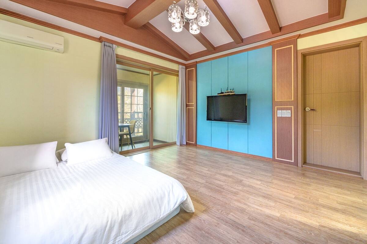 A bedroom with a bed, a TV mounted on the wall, and a sliding glass door leading to an outdoor area.