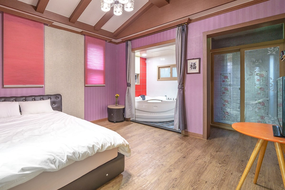 A bedroom with a large bed, a small round table, and a bathroom visible through an open door.