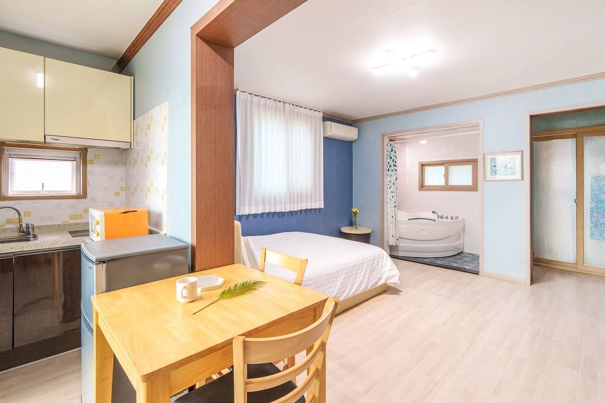 A compact hotel room with a kitchenette, a bed, a bathroom with a bathtub, and a TV.