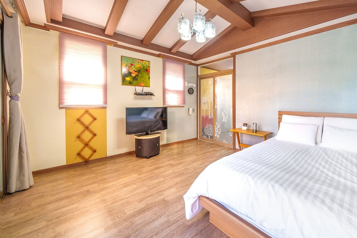 A bedroom with a wooden bed, a television, and a window with blinds.