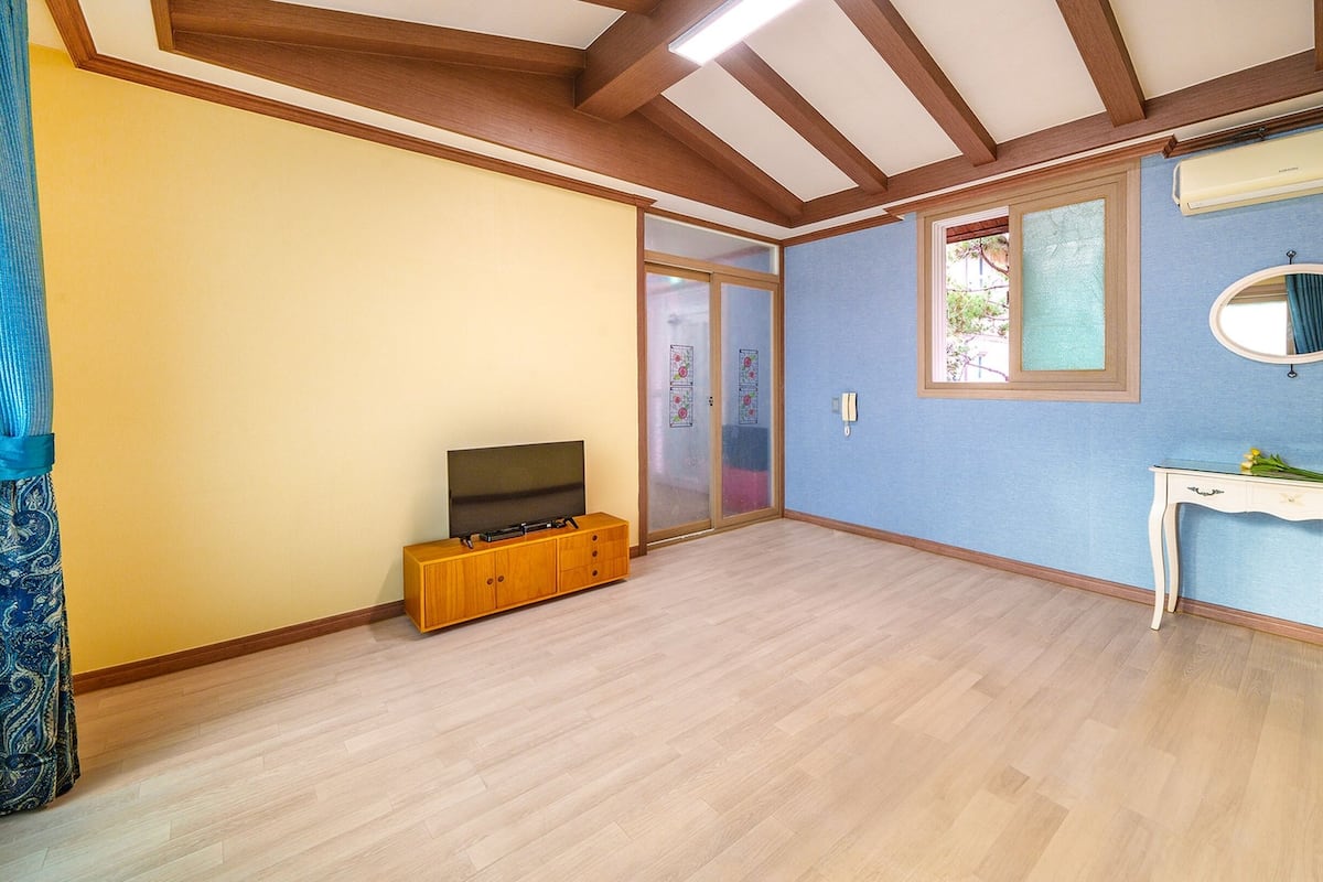 A room with wooden flooring, a TV on a wooden cabinet, a blue wall with a mirror, and a door leading outside.