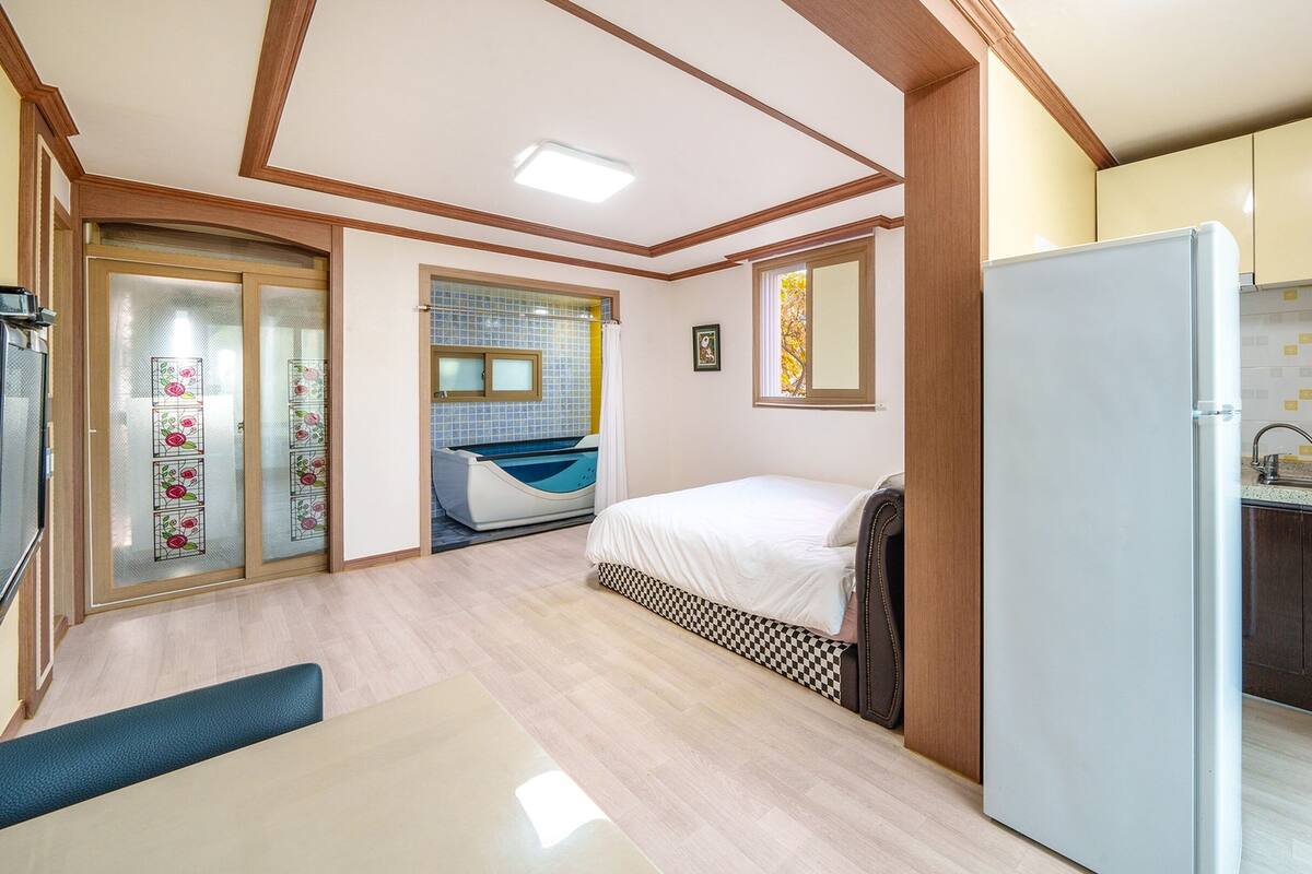 A compact room with a bed, a small kitchenette, and a shower area.