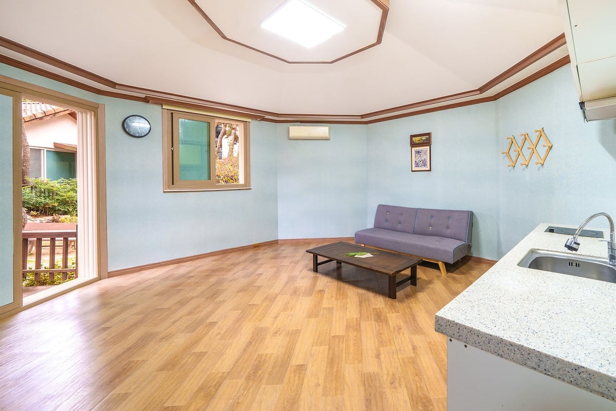 A living room with a wooden floor, a sofa, a coffee table, and a kitchen area with a sink and countertop.